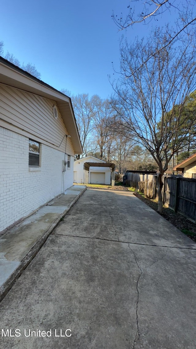 view of home's exterior with a garage, concrete driveway, an outbuilding, fence, and brick siding