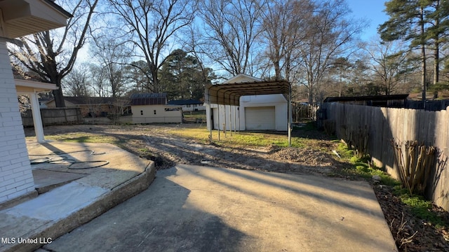 view of yard featuring a carport, fence, driveway, and an outdoor structure