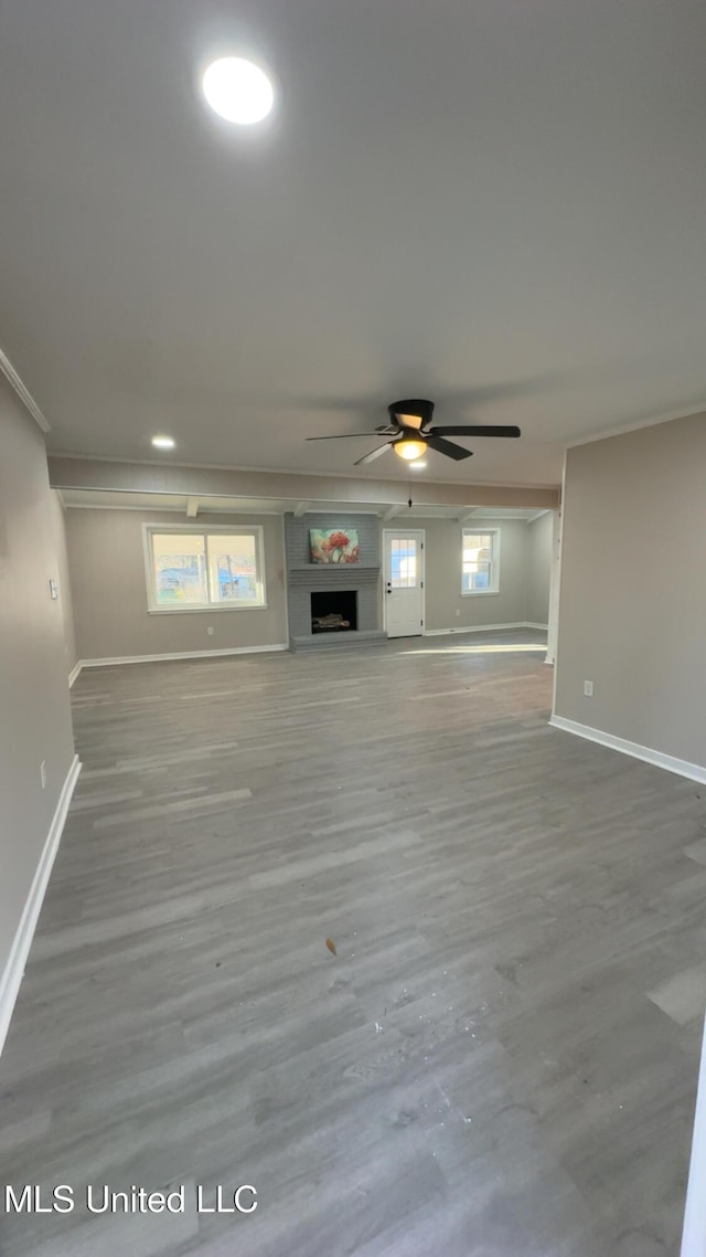 unfurnished living room featuring crown molding, a fireplace, baseboards, and wood finished floors