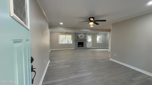 unfurnished living room featuring baseboards, a ceiling fan, wood finished floors, crown molding, and a fireplace