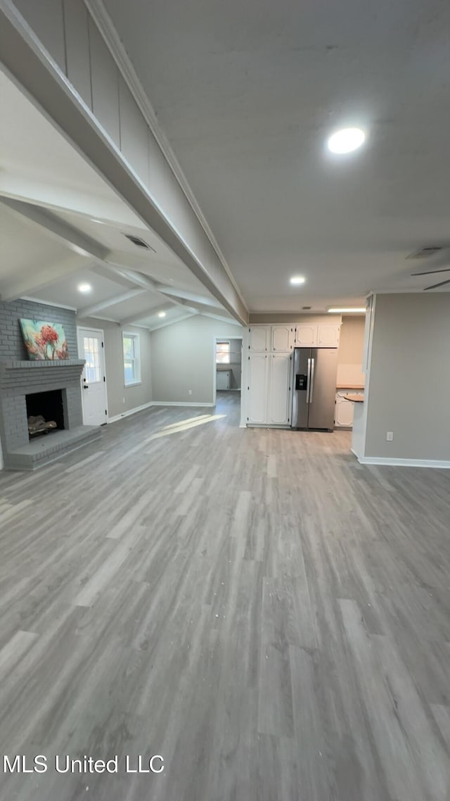 unfurnished living room featuring a brick fireplace, baseboards, visible vents, and light wood finished floors