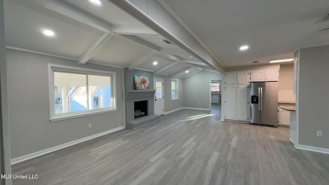 unfurnished living room featuring visible vents, baseboards, lofted ceiling with beams, light wood-style floors, and a fireplace