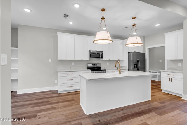 13379 Wash Fayard Rd, Biloxi, MS 39532 - kitchen with appliances with stainless steel finishes, light wood-style floors, a center island with sink, white cabinets, and decorative light fixtures
