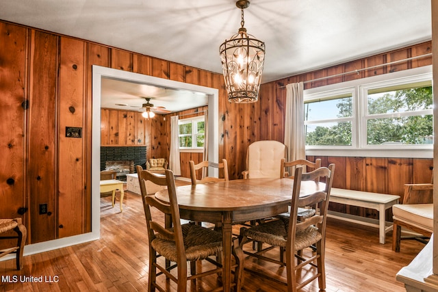 dining room featuring a fireplace, wooden walls, light wood-type flooring, and a wealth of natural light