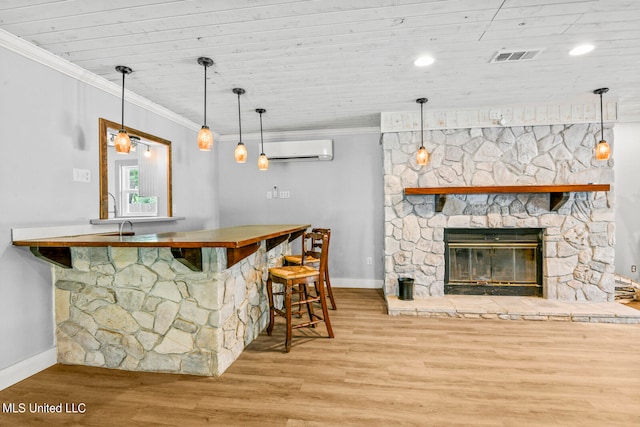 bar featuring a fireplace, an AC wall unit, hanging light fixtures, ornamental molding, and light hardwood / wood-style flooring