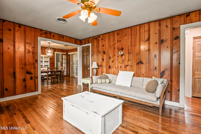 living room with wood walls, hardwood / wood-style floors, and ceiling fan with notable chandelier