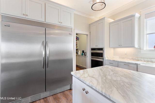 kitchen featuring appliances with stainless steel finishes, light stone counters, dark hardwood / wood-style floors, and white cabinets