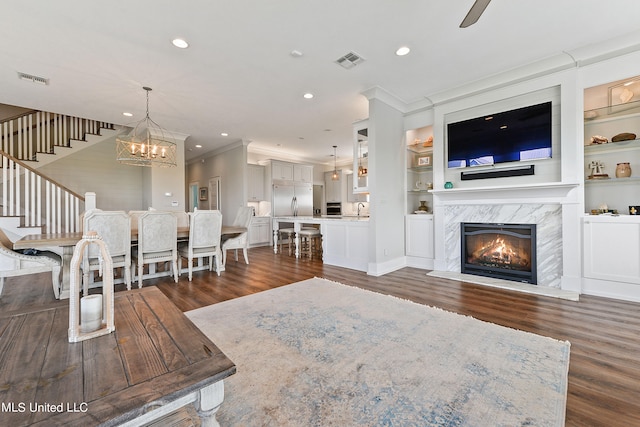 unfurnished living room featuring a premium fireplace, dark wood-type flooring, crown molding, and built in shelves