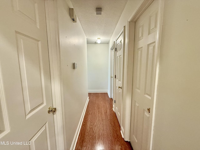 corridor featuring baseboards, dark wood-style floors, and a textured ceiling