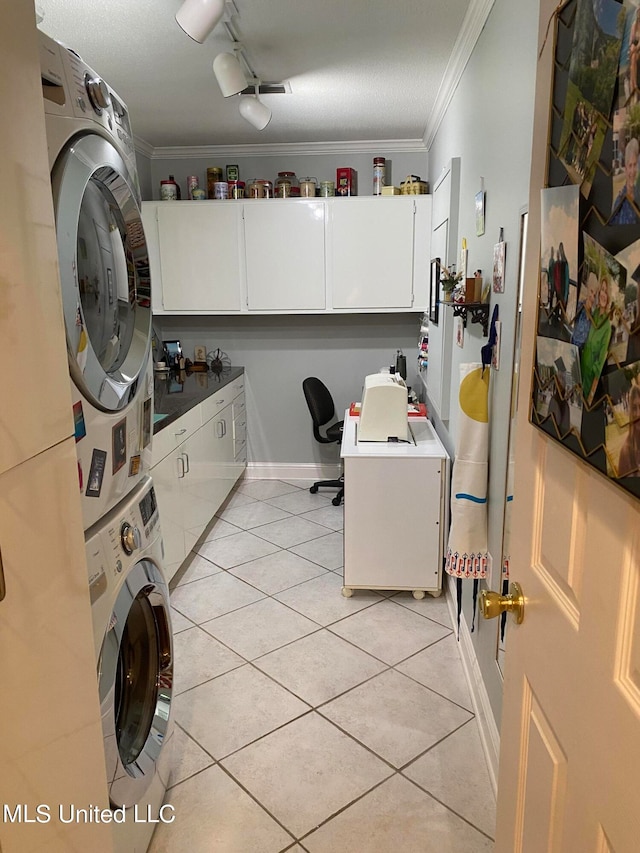 clothes washing area with cabinets, a textured ceiling, crown molding, stacked washer / drying machine, and light tile patterned flooring