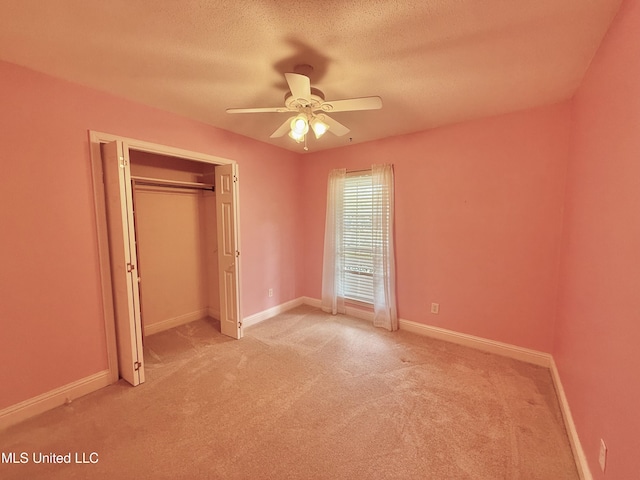 unfurnished bedroom featuring baseboards, a textured ceiling, a closet, and light colored carpet