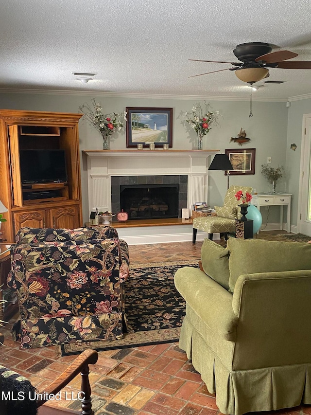 living room with a tiled fireplace, ceiling fan, a textured ceiling, and ornamental molding