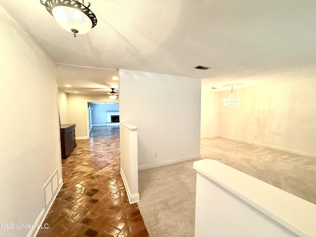 hallway with dark carpet, visible vents, baseboards, and an inviting chandelier