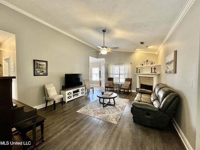 living room with dark wood-type flooring, ceiling fan, ornamental molding, a tiled fireplace, and vaulted ceiling