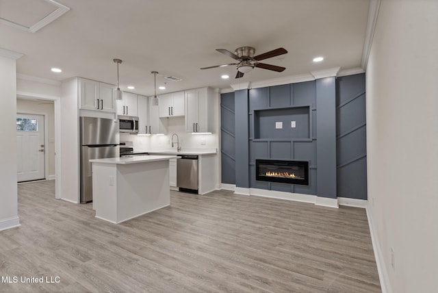 kitchen with stainless steel appliances, a glass covered fireplace, white cabinetry, and crown molding