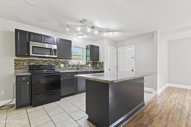 2607 Calle De Feliz St, Gautier, MS 39553 - kitchen with stainless steel microwave, black range with electric stovetop, decorative backsplash, and light stone countertops