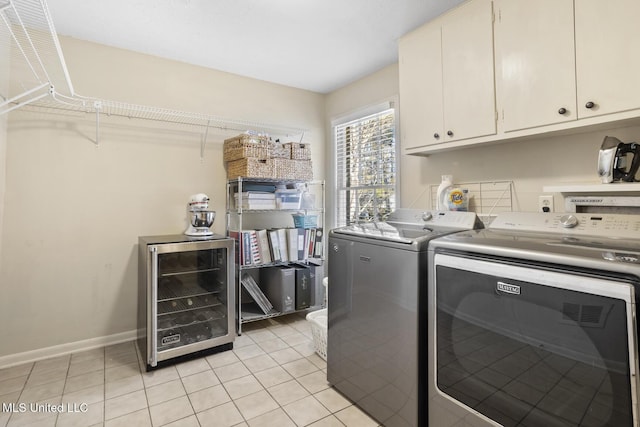 clothes washing area featuring cabinet space, beverage cooler, baseboards, washing machine and dryer, and light tile patterned flooring