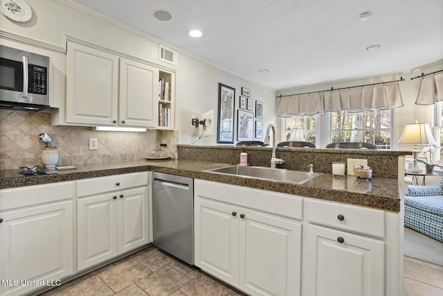 kitchen featuring tile countertops, a peninsula, a sink, stainless steel appliances, and backsplash