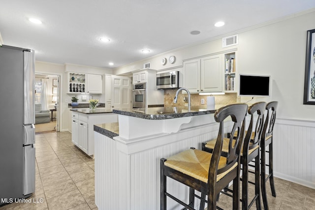 kitchen featuring open shelves, visible vents, appliances with stainless steel finishes, wainscoting, and a peninsula