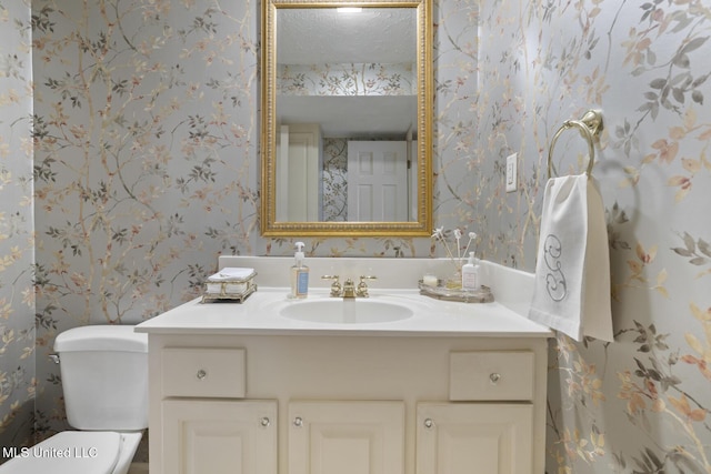 bathroom featuring a textured ceiling, vanity, toilet, and wallpapered walls