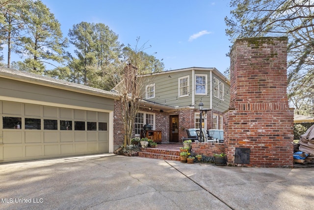 view of front facade with an attached garage, a chimney, concrete driveway, and brick siding