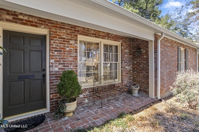 doorway to property featuring a porch and brick siding