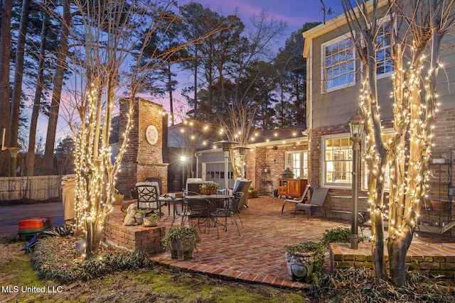 patio terrace at dusk with an outdoor brick fireplace and fence