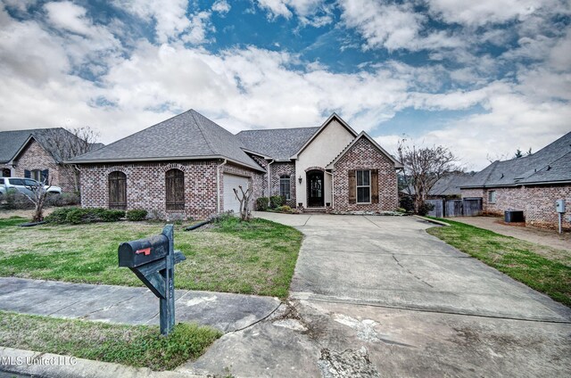 french provincial home with a garage, brick siding, a shingled roof, concrete driveway, and a front yard