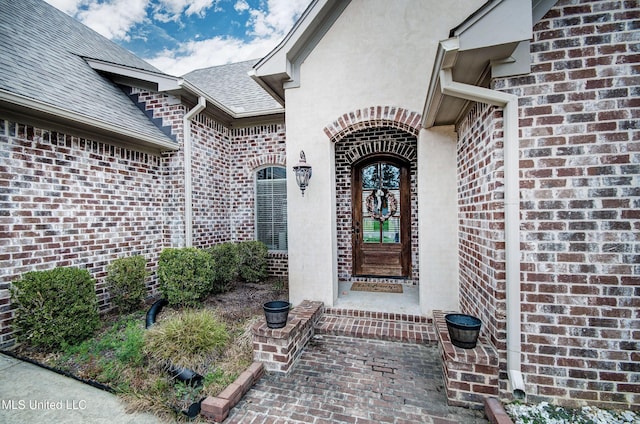 property entrance with stucco siding, brick siding, and roof with shingles