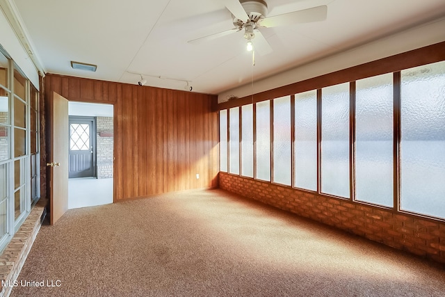 carpeted empty room featuring rail lighting, ceiling fan, and wooden walls