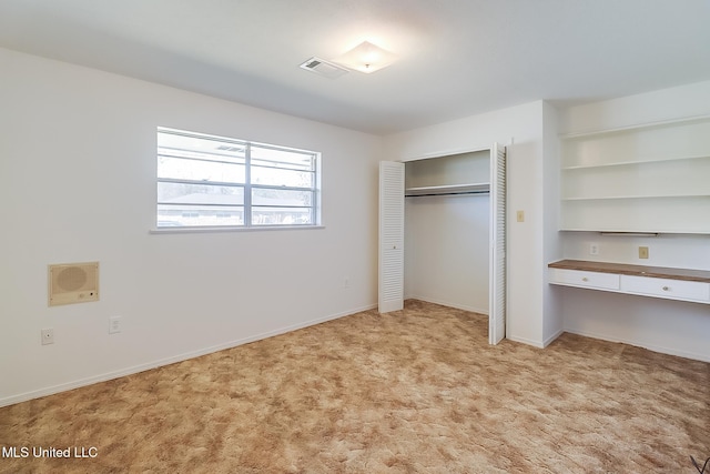 unfurnished bedroom with light carpet, built in desk, and a closet