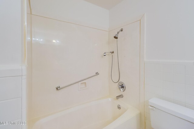 bathroom with tile walls, tiled shower / bath combo, and toilet