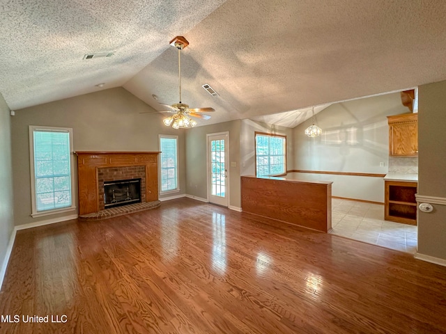 unfurnished living room with light wood-type flooring, a fireplace, a textured ceiling, ceiling fan, and vaulted ceiling