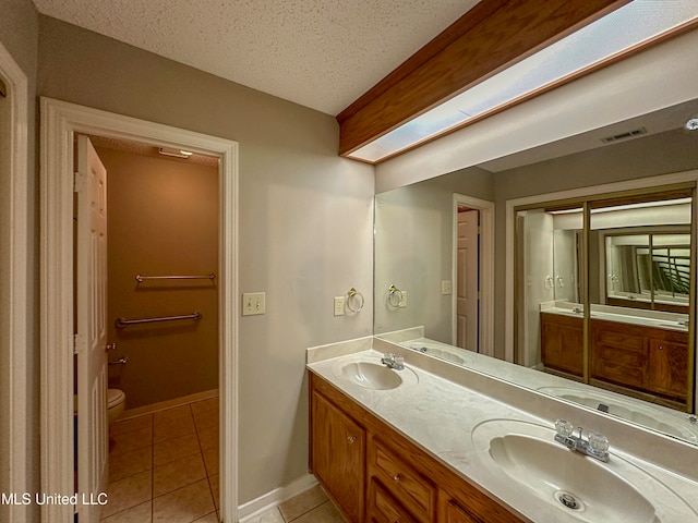 bathroom featuring a skylight, a textured ceiling, toilet, vanity, and tile patterned flooring