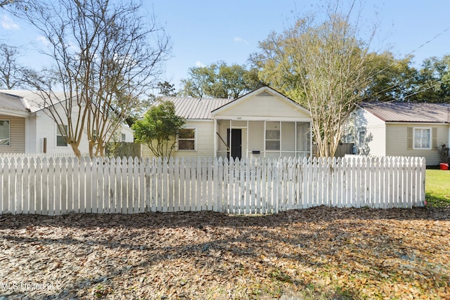 bungalow-style home with a fenced front yard, metal roof, and a sunroom