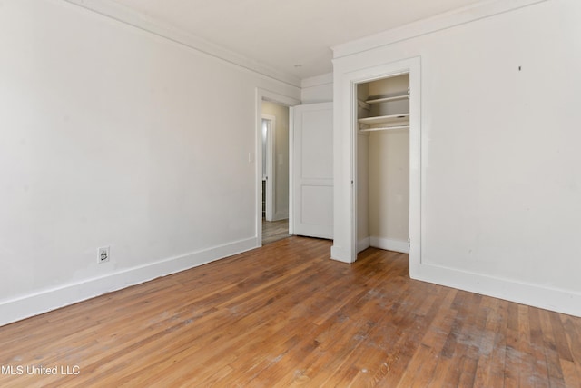 unfurnished bedroom featuring baseboards, wood-type flooring, a closet, and ornamental molding