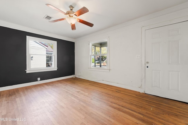 spare room with visible vents, ornamental molding, a ceiling fan, wood finished floors, and baseboards