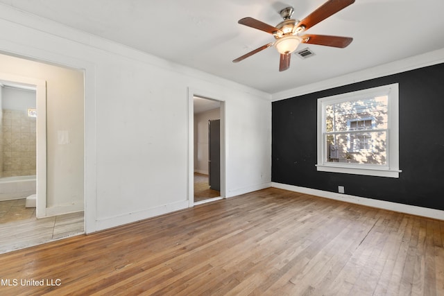 unfurnished bedroom featuring visible vents, baseboards, light wood-type flooring, ornamental molding, and ensuite bathroom