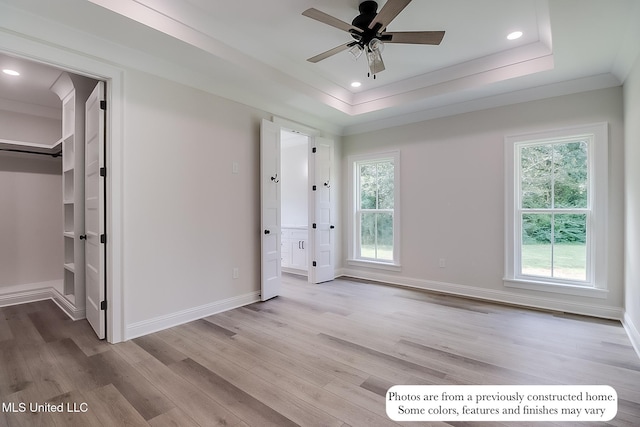 unfurnished bedroom featuring a tray ceiling, multiple windows, a walk in closet, and light wood-type flooring