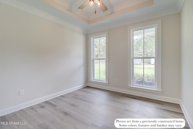 spare room with baseboards, ceiling fan, wood finished floors, and a tray ceiling