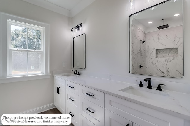 full bath with a sink, a marble finish shower, baseboards, and double vanity