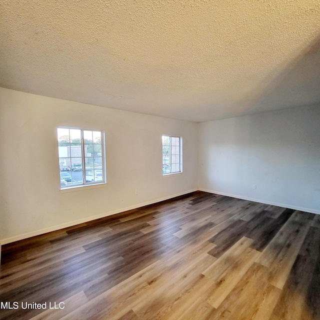 empty room with a wealth of natural light, a textured ceiling, and hardwood / wood-style flooring