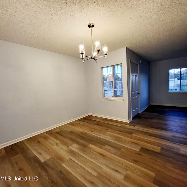 unfurnished dining area with dark hardwood / wood-style floors, a textured ceiling, and an inviting chandelier