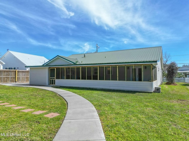 rear view of house with a sunroom, a lawn, metal roof, and fence