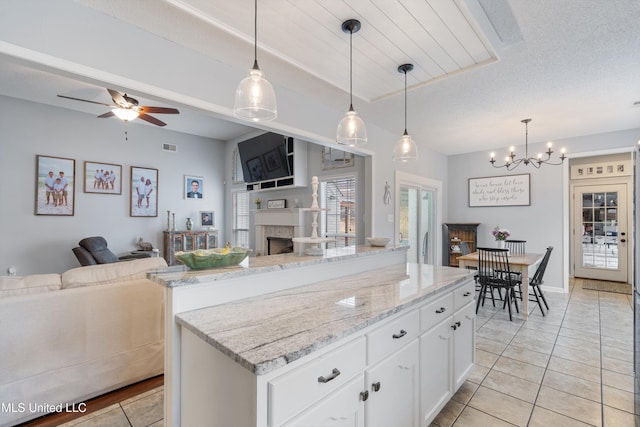 kitchen featuring light stone countertops, a center island, hanging light fixtures, and white cabinets