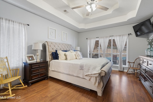 bedroom featuring ceiling fan, a tray ceiling, hardwood / wood-style floors, and access to exterior