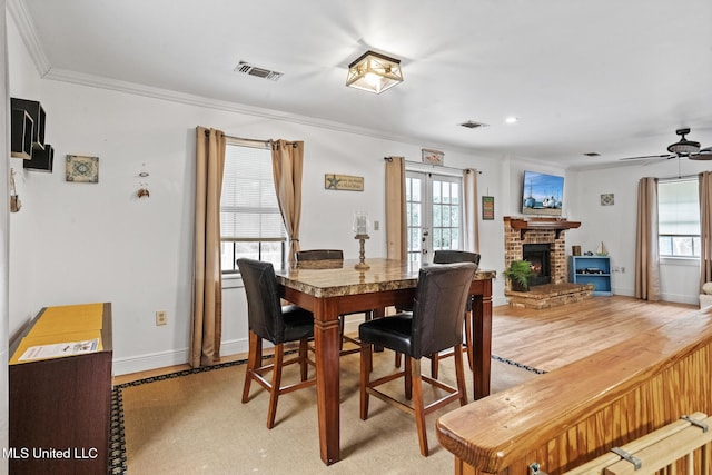 dining space with visible vents, light wood-style flooring, ornamental molding, french doors, and a brick fireplace