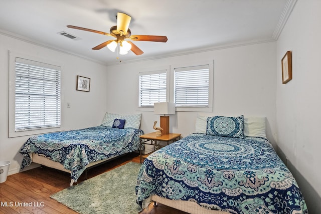 bedroom with wood finished floors, visible vents, crown molding, and multiple windows