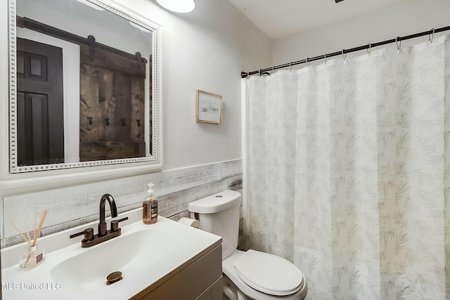 full bath with toilet, a wainscoted wall, a shower with curtain, vanity, and tile walls