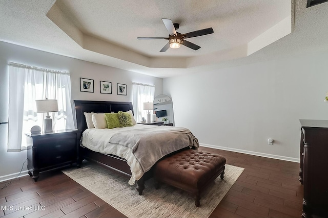 bedroom featuring dark wood-style floors, a textured ceiling, a raised ceiling, and baseboards